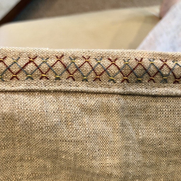 A piece of natural linen fabric with blue, red, and yellow herringbone stitch embroidery